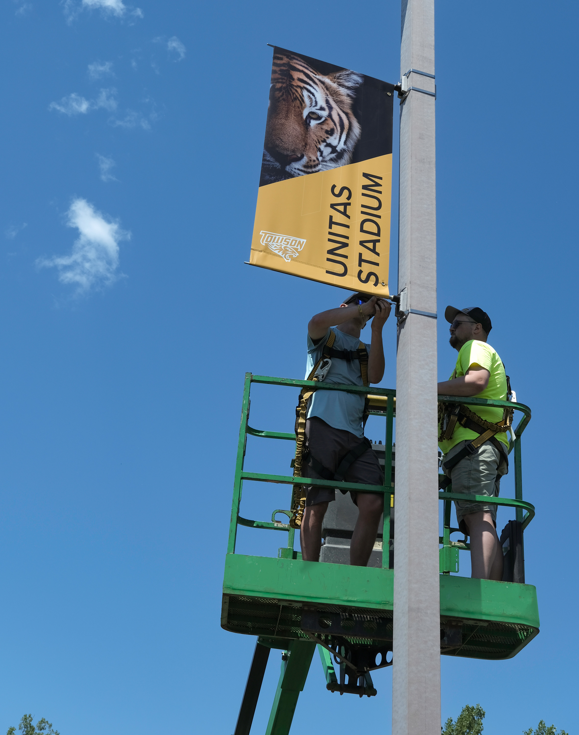 Two men on a lift installing an exterior pole banner.