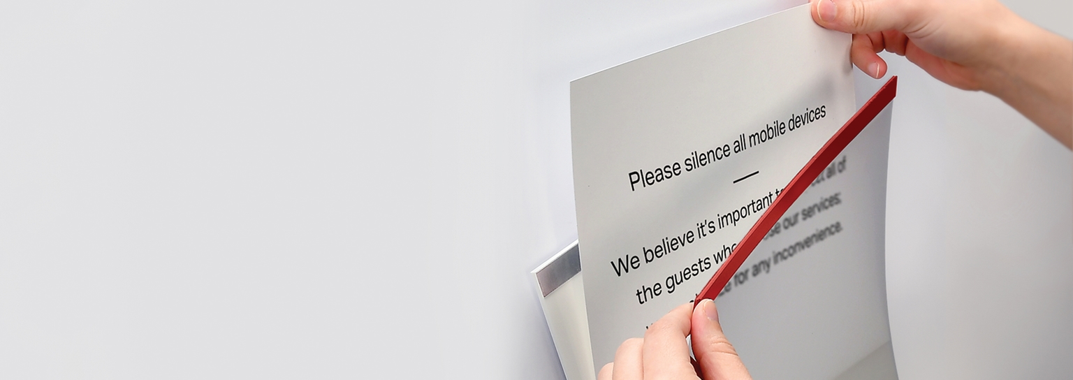 A photo of someone easily replacing a sheet of paper from a notice holder by simply pulling back the magnetic strip.