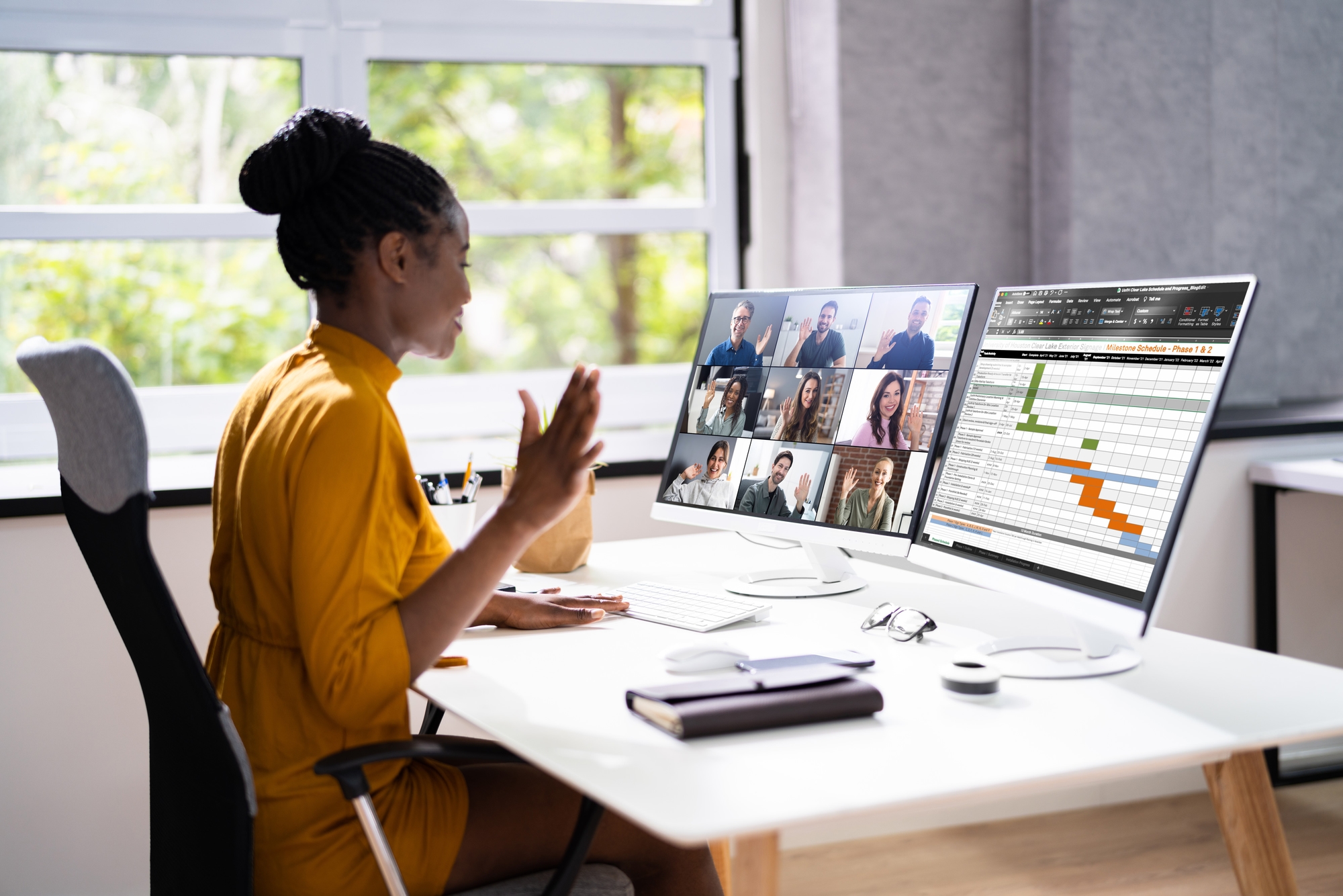 A Project Manager in a virtual conference call at her desk with a project schedule on her monitor.