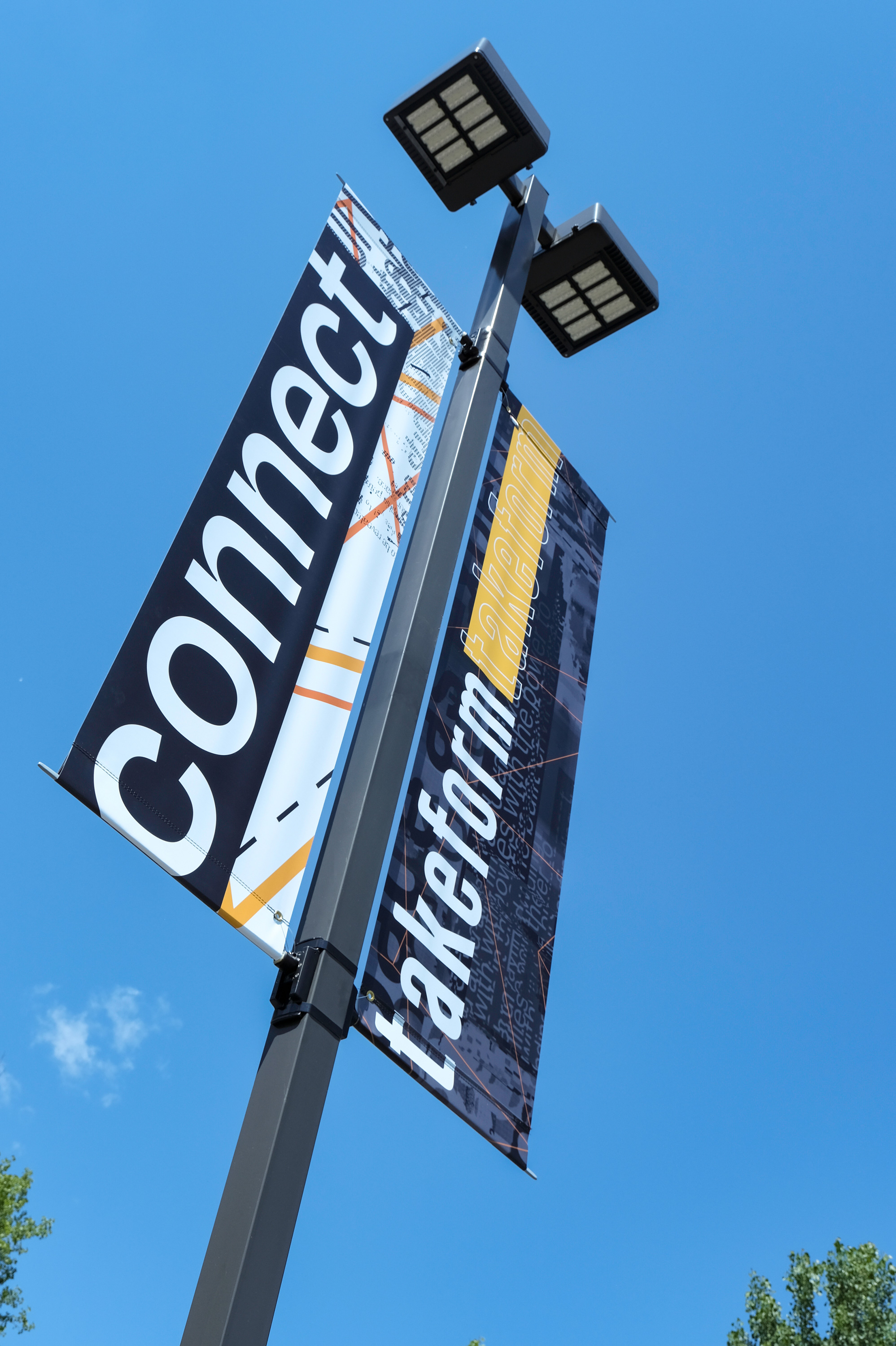 Two custom printed branded exterior banners attached to a single pole with blue skies.