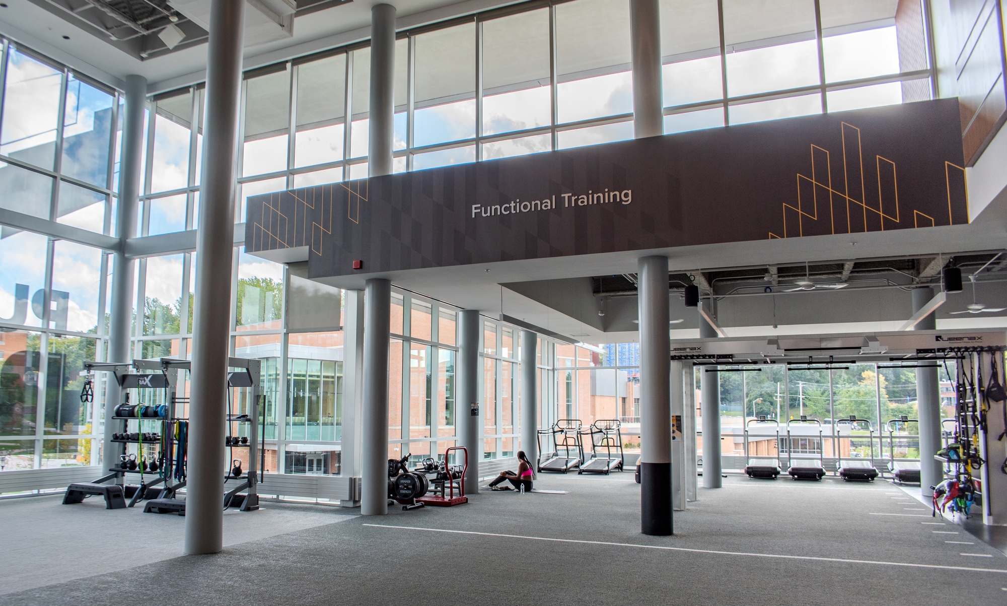 A woman stretching in a large open training facility branded with custom wallcovering and dimensional letters.