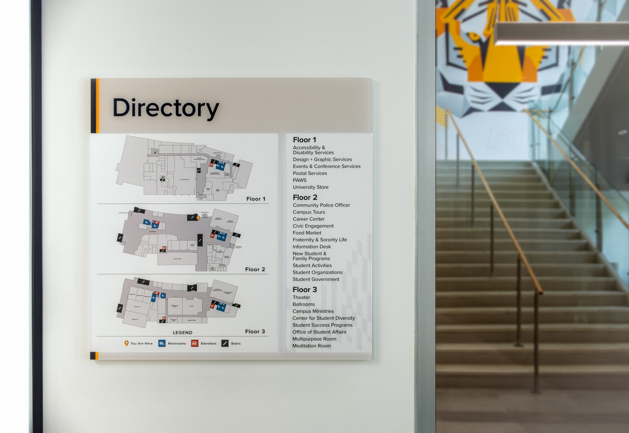 A Vivid interior directory sign an a wall beside a stairwell in a college building.