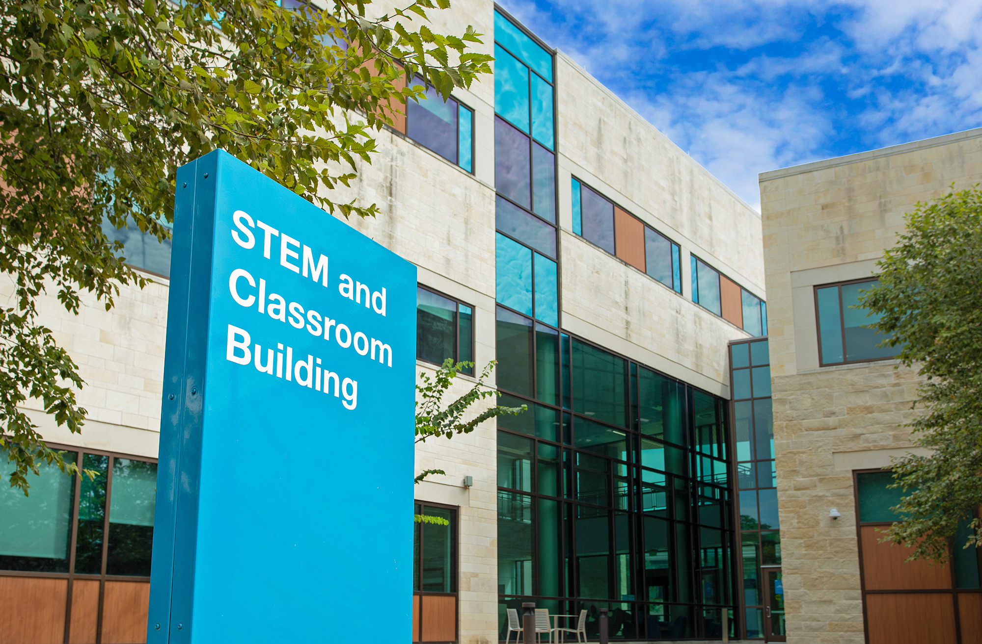 A porcelain coated exterior building ID sign complimenting a college building that stands behind the sign.