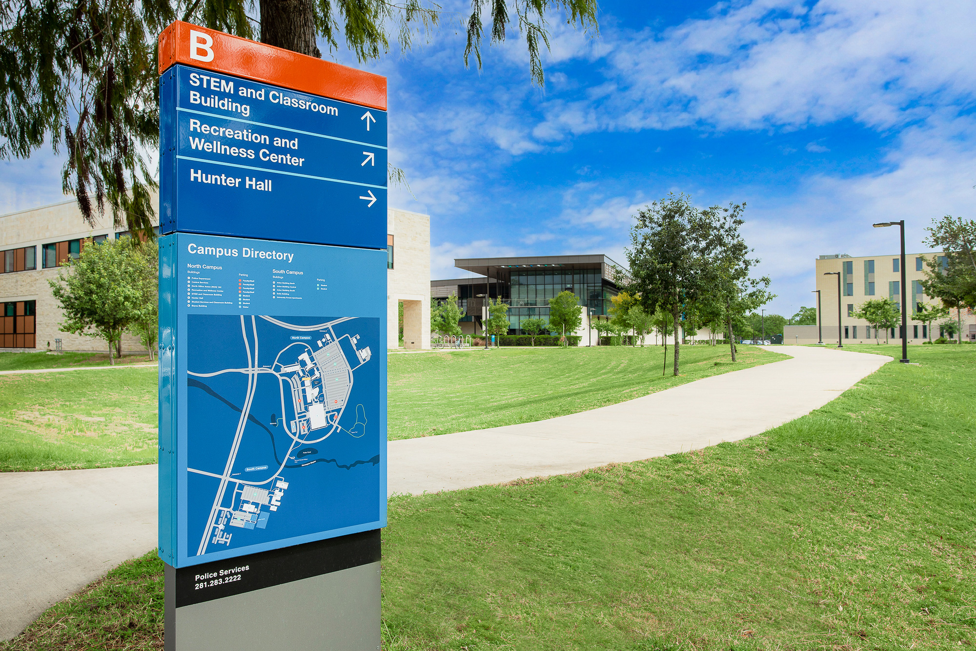 A porcelain coated exterior wayfinding sign stands next to a sidewalk on a college campus.
